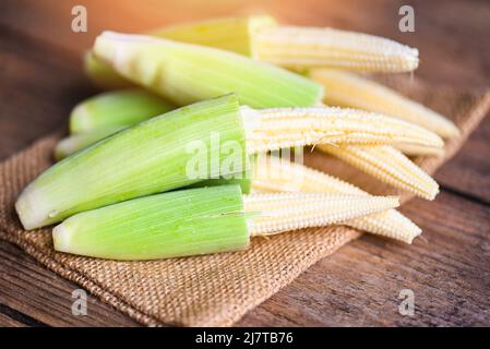 Baby corn on the sack, Fresh young baby corn for cooking health food, Close up raw organic baby corn on wooden background. Stock Photo