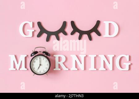 Creative good morning concept. White letters, black eyeleshes and alarm clock on pink background. Top view, Flat lay. Greeting card. Stock Photo
