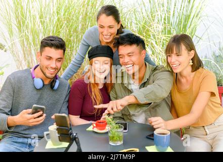 Group of delightful diverse people sitting at table in street cafe and speaking with friends during video chat Stock Photo