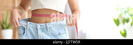 Young woman in loose jeans measuring waist at home. Diet concept Stock Photo