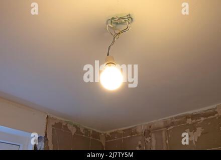 Lightbulb hanging temporarily on a ceiling, bringing light in the darkness Stock Photo