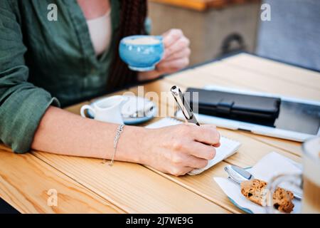 To do list, planning for freelancers. Woman holding pens and papers making notes and drinking coffee in street cafe. Close-up of female freelancer Stock Photo