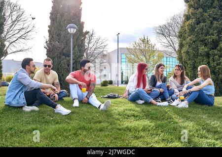 Group of guys sitting in a park next to a group of girls, drinking and hanging out on a sunny day. High quality photo Stock Photo