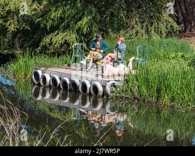 Beervelde, Belgium, 08 May 2022, two women are sitting in the sun on the waterfront on a raft enjoying a cup of coffee and you can see their reflectio Stock Photo