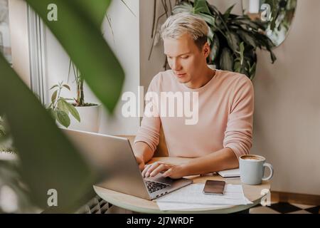 Man works in the workplace with laptop and and drinks coffee in an eco cafe with plants Stock Photo