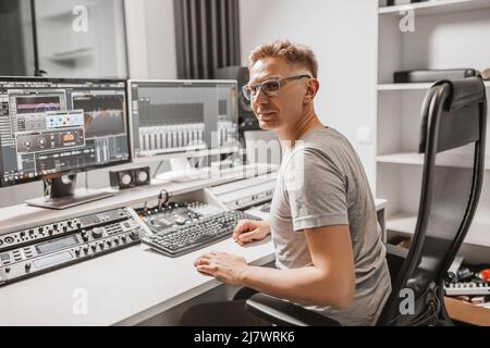 Man working in music studio using computer wearing glasses. Sound engineer working and mixing track. Programmer watching at display of it while listen Stock Photo