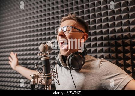 The vocalist sings in the studio in a microphone. Man in headphones writes a podcast, an audiobook. Artist, recording an album, working with the label Stock Photo