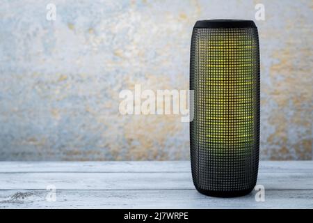 A portable music column on wooden gray background. Musical wireless speaker with yellow glow. Sound system. Single object. Copy, text space Stock Photo