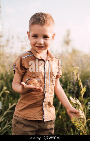 A little boy stands in the grass in nature and holds a snail in his hand Stock Photo