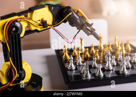Closeup yellow robot arm playing move chess on chessboard, STEM education E-learning, Technology science robot education concept Stock Photo