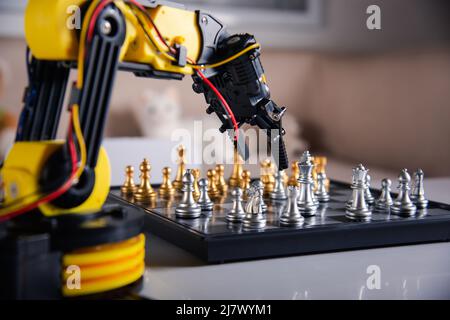 Closeup yellow robot arm playing move chess on chessboard, STEM education E-learning, Technology science robot education concept Stock Photo