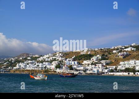 Boats on water in the port of Chora, Mykonos, with white traditional houses in the back Stock Photo