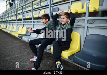 Two brothers support their favorite team, sitting on the sports podium at the stadium. Stock Photo