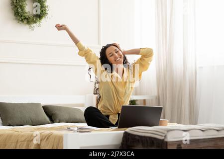 Smiling Arab woman stretching back sitting on bed Stock Photo