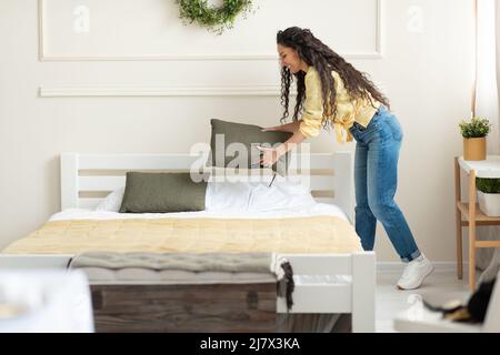 Happy millennial young woman making bed after wake up Stock Photo