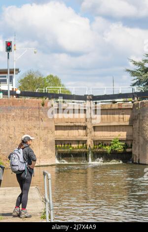 Rear view of a woman looking at a set of closed automated river lock gates, focus is on the woman hiker Stock Photo