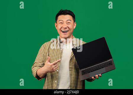 New website. Excited mature asian man holding laptop computer with blank screen and pointing at monitor, mockup Stock Photo