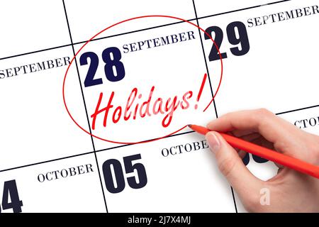28th day of September. Hand drawing a red circle and writing the text Holidays on the calendar date 28 September . Important date. Autumn month, day o Stock Photo