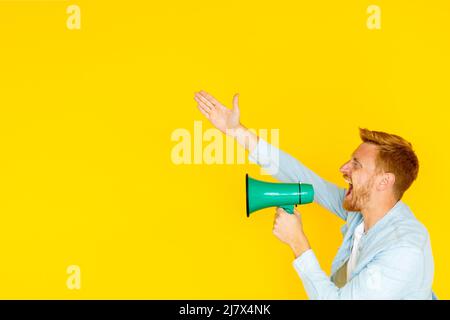 Excited young man screaming in megaphone over isolated yellow background Stock Photo