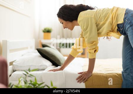 Portrait of cheerful young woman making bed after wake up Stock Photo