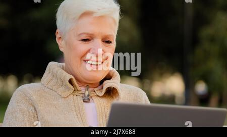 Happy aged woman working at laptop smiling senior female of retirement age using computer browsing or surfing internet, reading news online, excited Stock Photo