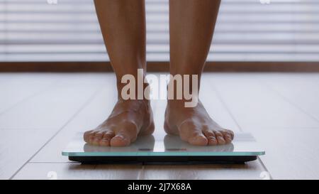 Close-up slender female legs unrecognizable woman standing barefoot in bathroom stepping on electronic scales checking weight after fat burning Stock Photo