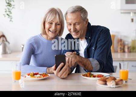 Happy senior couple using smartphone while having breakfast Stock Photo