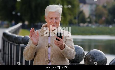 Happy senior woman of retirement age making video call, looking at smartphone camera. Attractive old mature female uses modern gadget wireless Stock Photo