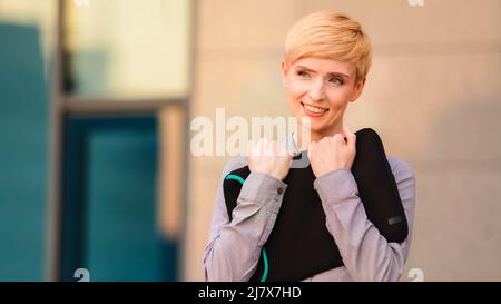 Happy mature adult business woman boss leader stands outdoors near company office building holds laptop in case hugs embraces computer rejoices at Stock Photo