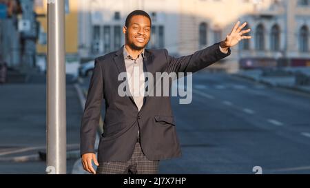 Modern businessman or manager gesturing to give signal to car driver on the street in big city. Taxi service concept. Attractive African American Stock Photo