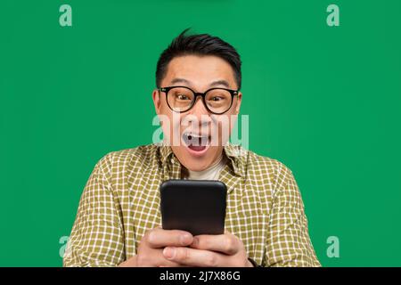 Overjoyed mature asian man in glasses looking at smartphone in shock, amazed at promo sale or huge discount Stock Photo
