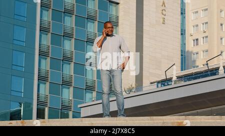 Adult mature african man answering phone, holding cellphone, surprised glad to hear good news. Elderly black businessman in casual clothes received Stock Photo