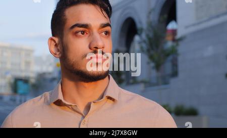 Close up view of good looking hispanic business man in shirt looking away dreaming standing in city with serious face. Portrait of millennial guy Stock Photo