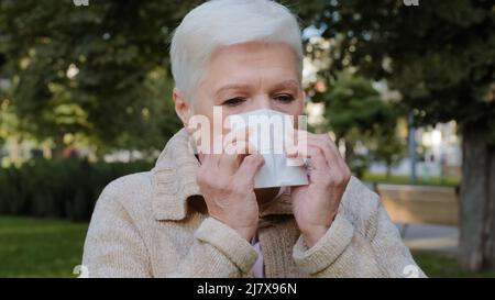 Allergic middle-aged lady feels unwell having flu symptom, ill old mature woman hold tissue sneezing got fever caught cold blowing running nose in Stock Photo