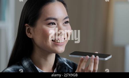 Portrait asian korean woman girl recording voice recognition message on speakerphone lady female at home using virtual assistant app sets reminder on Stock Photo