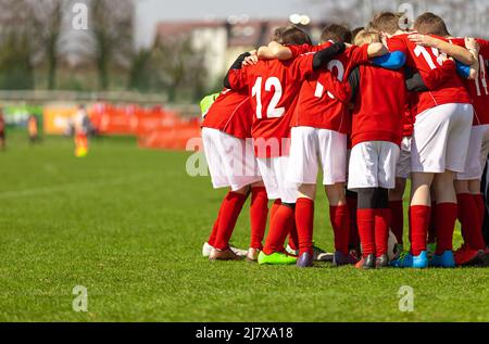Kids soccer team with coach in group huddle before the match. Elementary age children are listening together to coach motivational speech. Boys in red Stock Photo