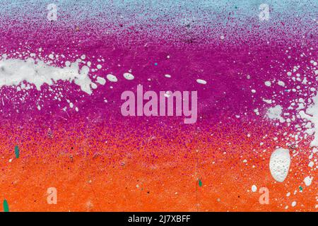 Macro close-up of wall spray painted with purple, orange & light blue/turquoise. White spray paint splashes. Abstract splattered graffiti background. Stock Photo