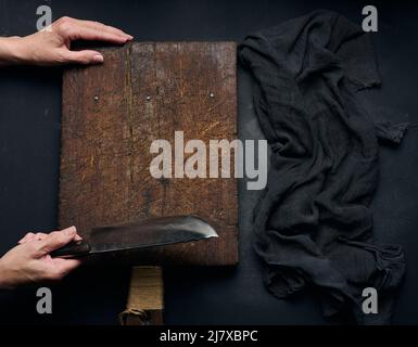 empty brown rectangular wooden cutting board, woman holding big knife over black table, top view Stock Photo