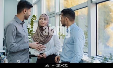 Multiethnic colleagues arab muslim woman in hijab and two Indian millennial male discuss corporate task. Diverse workers businesspeople working Stock Photo