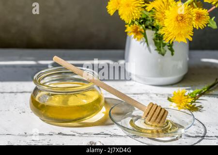 Dandelion honey in jar on the white wooden table with flowers and honey spindle spoon on glass platter Stock Photo