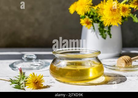 Dandelion honey in jar on the white wooden table with flowers and honey spindle spoon on glass platter Stock Photo