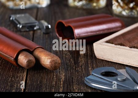Two Cuban cigars in a leather case with a wooden box on an old brown table top. Glass of whiskey on a blurred background. Stock Photo