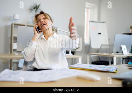 Emotional business woman talking on the phone and pointing with her hand at the camera Stock Photo