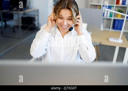 Cheerful call center office female employee in headset with  talking during video call Stock Photo