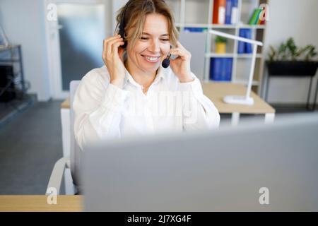 Laughing businesswoman wearing headset talking to caller in customer services department Stock Photo