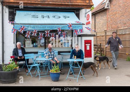 Dunsfold village shop, Surrey, England, UK, on the day of the annual fete with men sitting outside having drinks Stock Photo