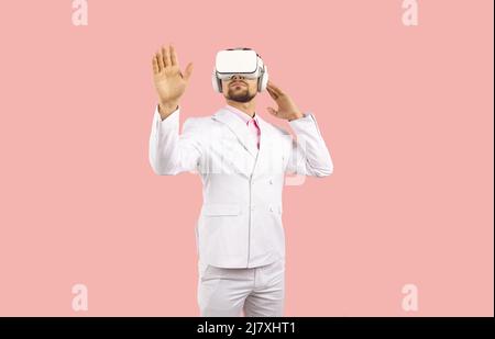 Young man standing on pink background experiencing virtual reality in modern VR headset Stock Photo
