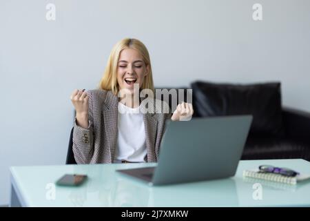 Happy excited woman at home workstation triumphing with raised hands Stock Photo