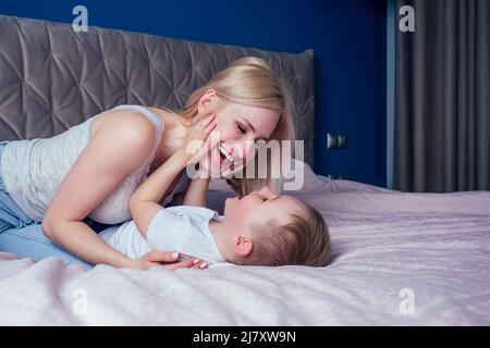 Family having fun together at the weekend together.Mother and two child on bed. blonde mom and baby boys playing in morning bedroom. Parent and little Stock Photo