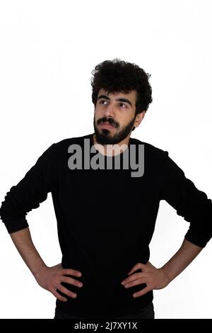 Curly haired young male in black sweater stands with his hands on his hips. Isolated on white background Stock Photo